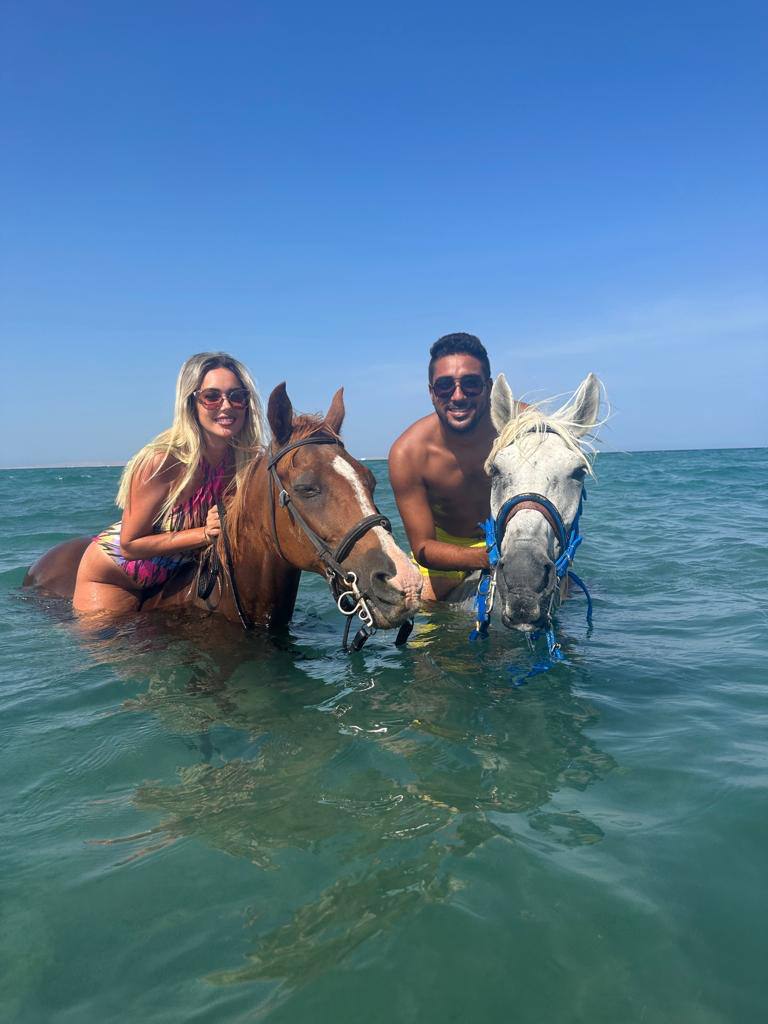 Two guests riding horses through shallow turquoise water off Hurghada